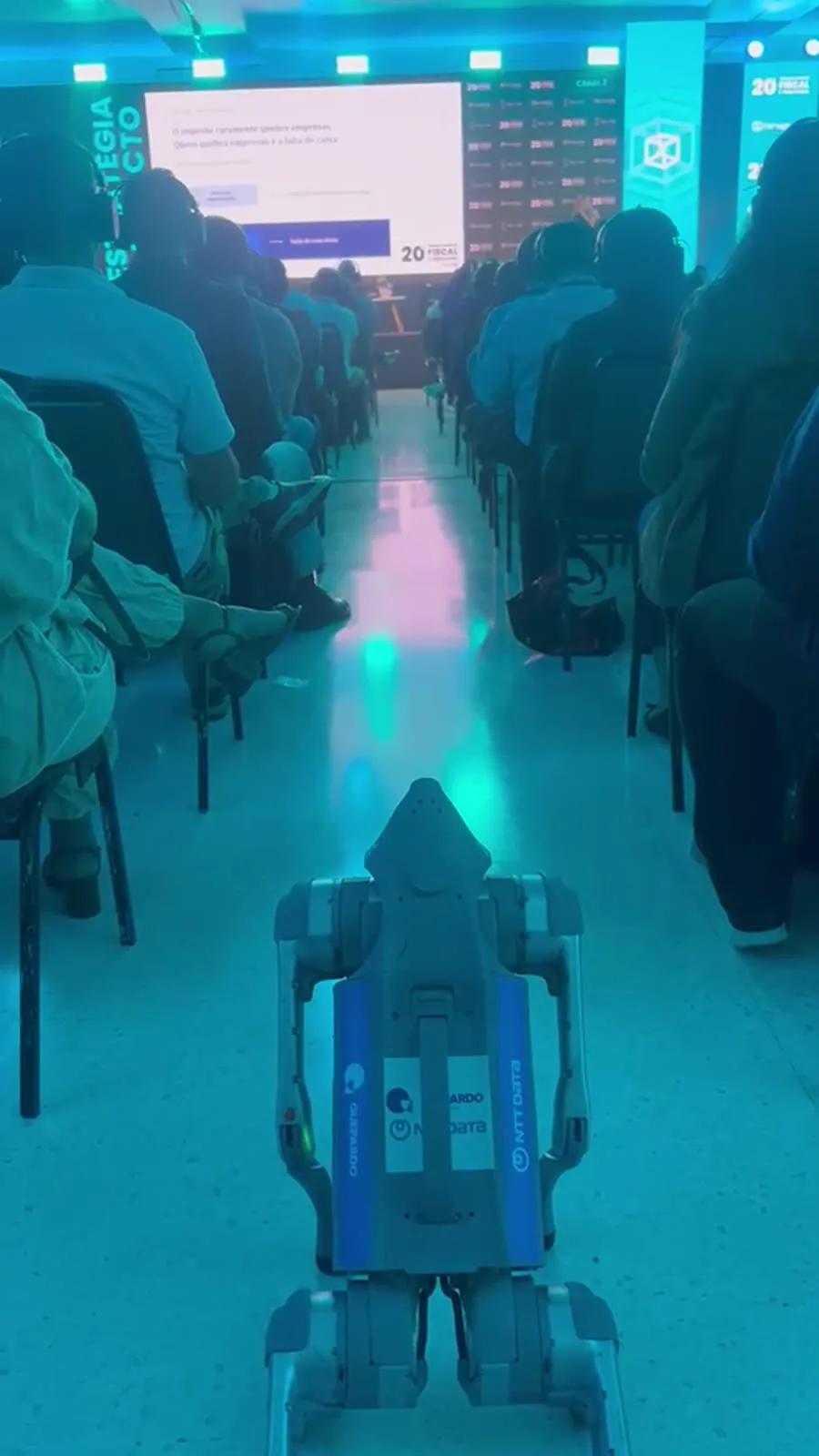 Cão robô Go2 Pro caminhando pelo corredor entre a plateia a caminho do palco